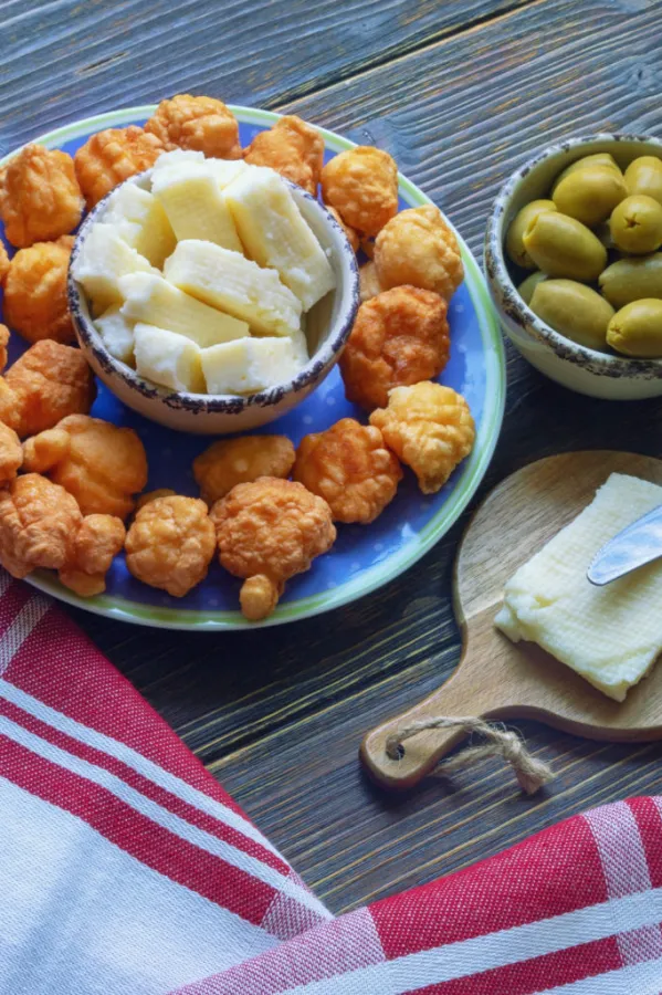 Balkan cuisine. Priganice (small fried cakes, donuts) with local cheese and olives on dark rustic table. Copy space