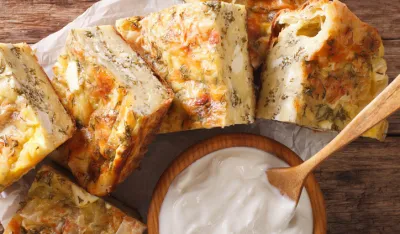 Serbian pie Gibanica with cheese, eggs and greens close-up on the table. Horizontal view from above<br>