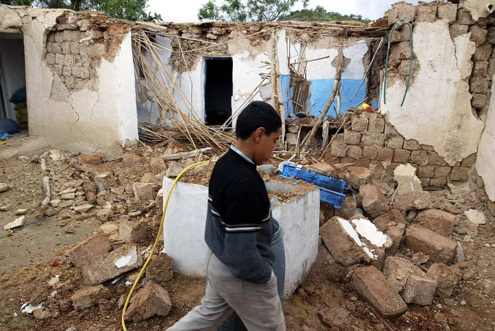 Alaoui Abdelkarim walks by rubble of a destroyed house in the village of Ait-Kamra, Wednesday Feb.25, 2004. A strong earthquake Tuesday killed more than 550 people in a poor region of northern Morocco. Many survivors braved a chilly, wet night without a home in makeshift tents.The quake shook areas near the coastal city of Al Hoceima, an isolated but picturesque area between the Rif Mountains and the Mediterranean Sea. (AP Photo/Michel Spingler)