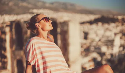 Nice peaceful girl sitting on the high point and enjoying beautiful amazing view on an ancient city in Greece. Happy travel to Europe.