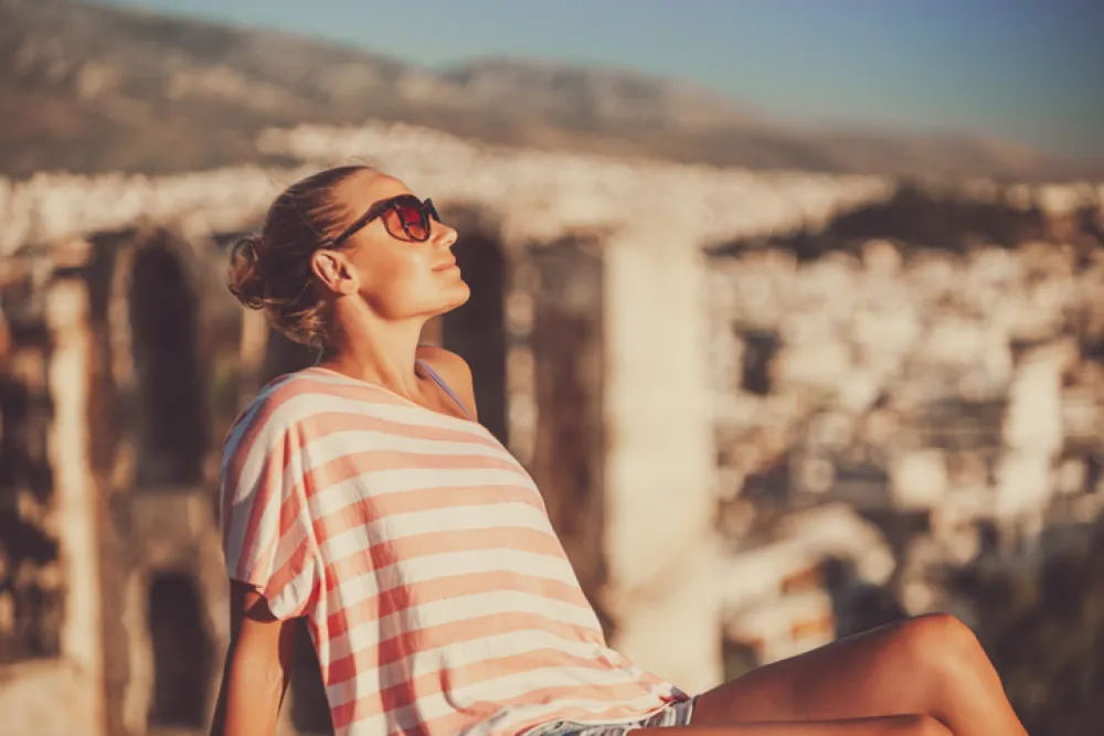 Nice peaceful girl sitting on the high point and enjoying beautiful amazing view on an ancient city in Greece. Happy travel to Europe.