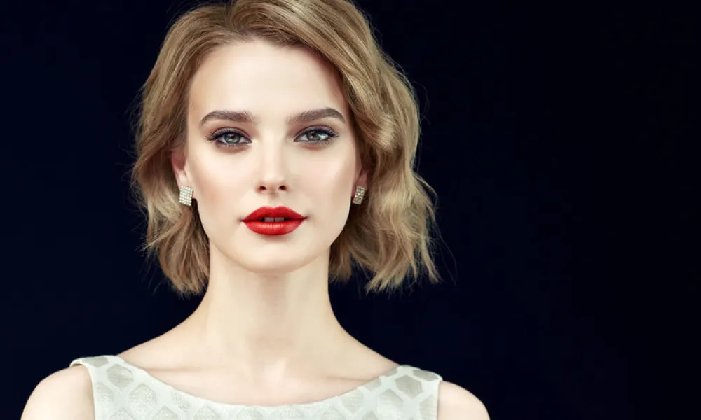 Portrait of beautifully looking young light blonde haired woman, dressed in a delicate evening makeup.Perfect model straightly gazing by kind, tender look at viewer. Beauty, elegance, hairstyling and cosmetic.
