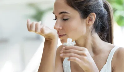 Shot of a cheerful woman girl holding a bottle of essential oil while testing it sitting on a couch at home.parfem k