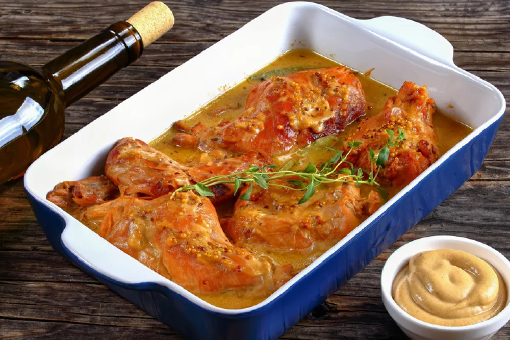 appetizing Rabbit Cooked in mustard sauce or lapin a la moutarde in gratin dish on wooden table with bottle of wine and garlic on background, authentic french recipe, view from above, close-up