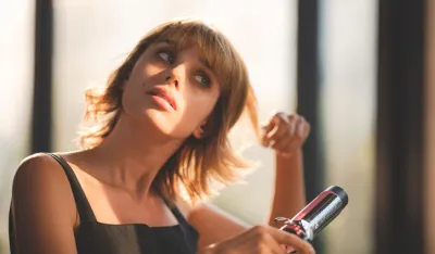 Young beautiful blonde woman with short hair using electronic curling iron styling her hair for fashion and trying new lifestyle at home by looking at self in mirror
