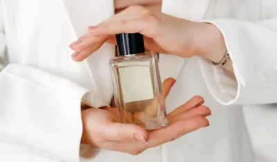 Hands of a beautiful young woman with a bottle of floral perfume on a light background