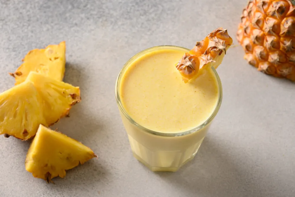Traditional Pineapple lassie or smoothie on gray background. Traditional Asian beverage of pineapple, yogurt and ice. View from above. Copy space.