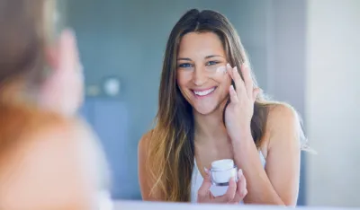 Portrait of a beautiful young woman applying moisturizer to her face while looking in the mirror