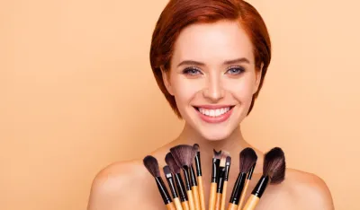 Close-up portrait of nice cute lovely attractive charming cheerful cheery girl smooth clean clear perfect shine skin holding in hands brushes isolated over beige background.