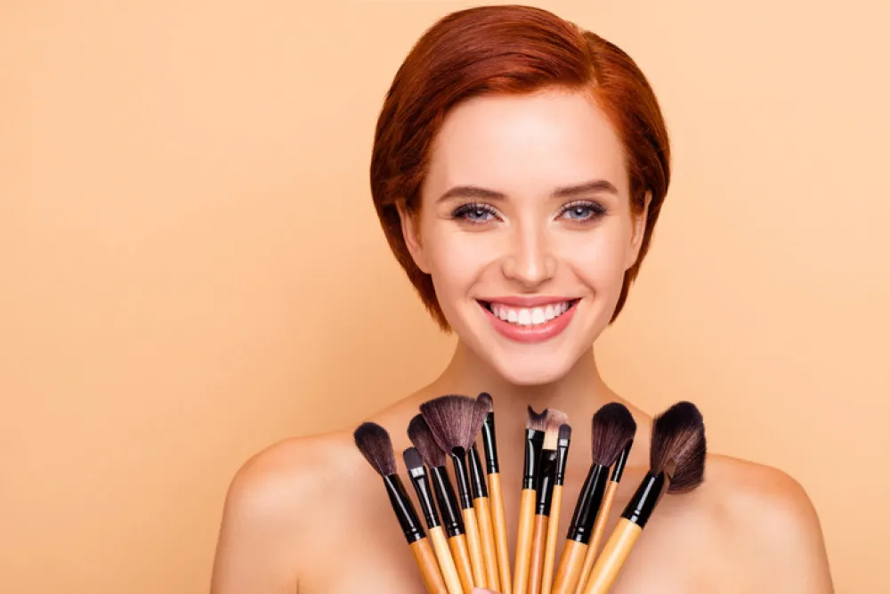 Close-up portrait of nice cute lovely attractive charming cheerful cheery girl smooth clean clear perfect shine skin holding in hands brushes isolated over beige background.