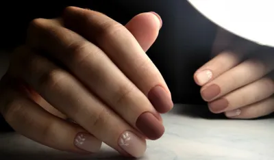 Gentle coffee manicure with white design. Short square nails with brown-beige coating and the design of twigs.