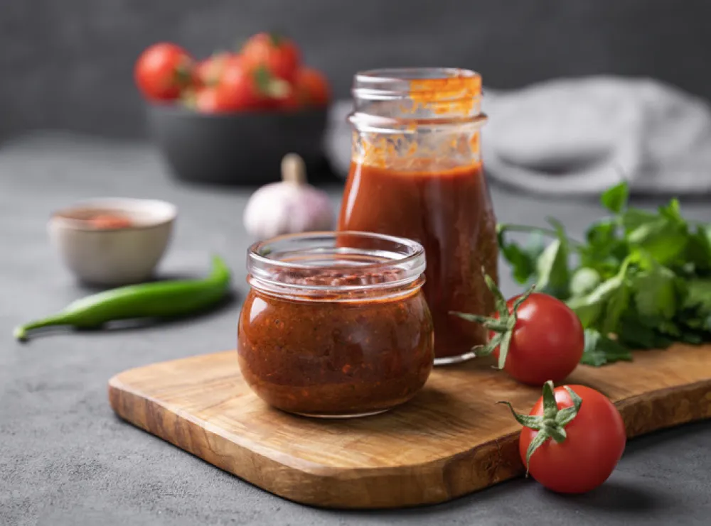 Tomato paste of hot pepper marinara with garlic, tomatoes and herbs in jars on a wooden board on a dark background. Traditional homemade food.