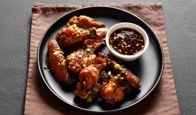 Sticky honey-soy chicken wings on plate over dark stone background. Close up view