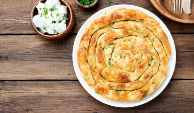 Traditional feta cheese phyllo pastry pie on wooden background.