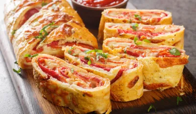Italian food Pizza roll stromboli with cheese, salami and tomatoes closeup on the wooden board on the table. Horizontal<br>