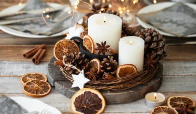 Rustic decor for christmas holiday family dinner. Center piece with white candle, dry orange, cones, cotton. Zero waste eco friendly home decoration. Cozy atmosphere, wooden background. Close up