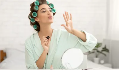 Pretty Millennial Lady Blowing At Nails Applying Fingernail Polish Sitting In Modern Bedroom Making Manicure At Home. Female Beauty Care And Cosmetics Concept. Selective Focus