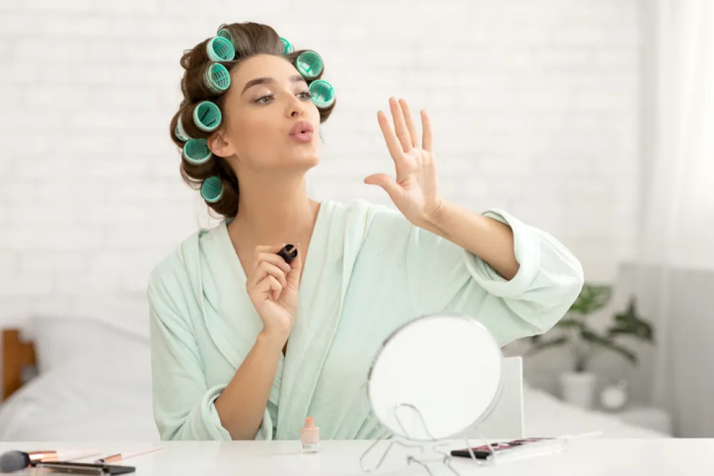 Pretty Millennial Lady Blowing At Nails Applying Fingernail Polish Sitting In Modern Bedroom Making Manicure At Home. Female Beauty Care And Cosmetics Concept. Selective Focus