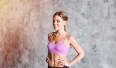 Young pretty woman dressed in a pink top with her hands on hips in the grey background sunlight effect