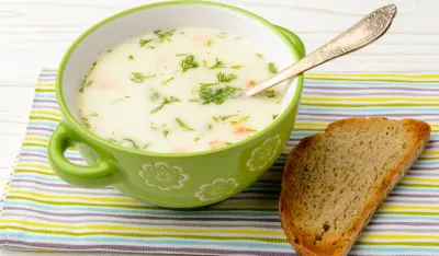 Cheese soup in green bowl on white wooden table.