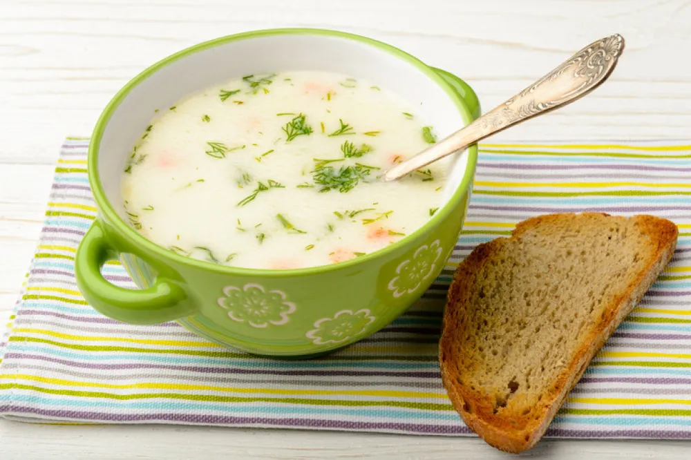 Cheese soup in green bowl on white wooden table.