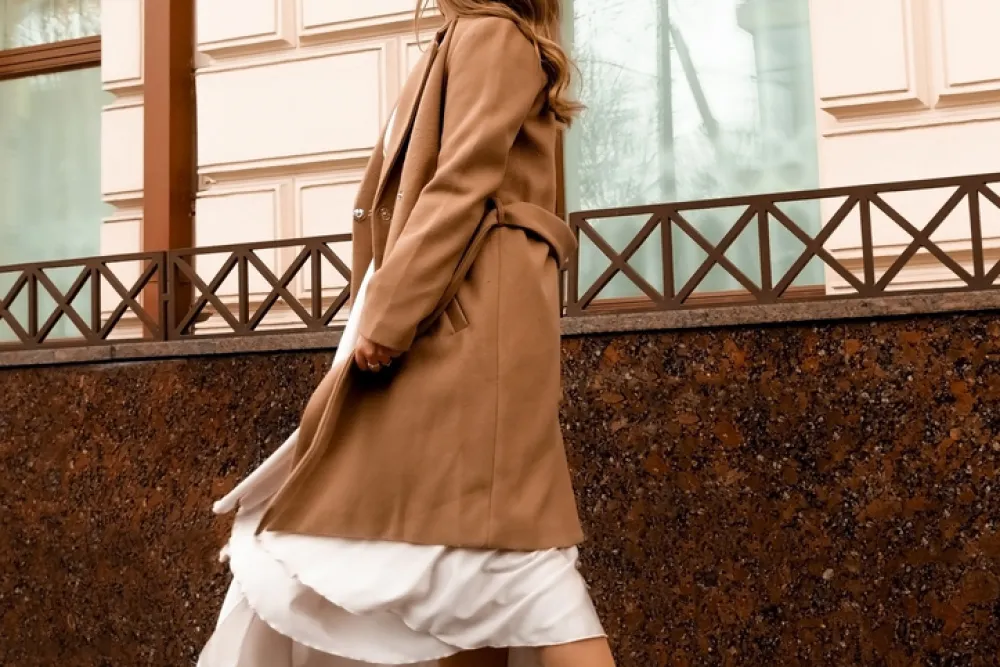 girl in brown coat and beige dress is spinning in the street