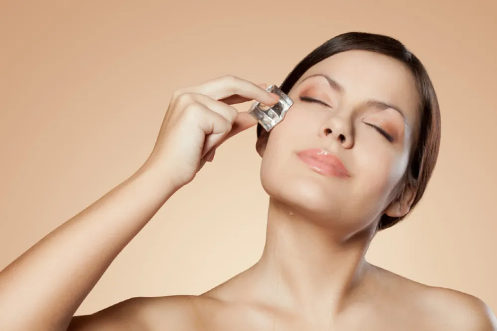 brunette woman holding ice cube on her face