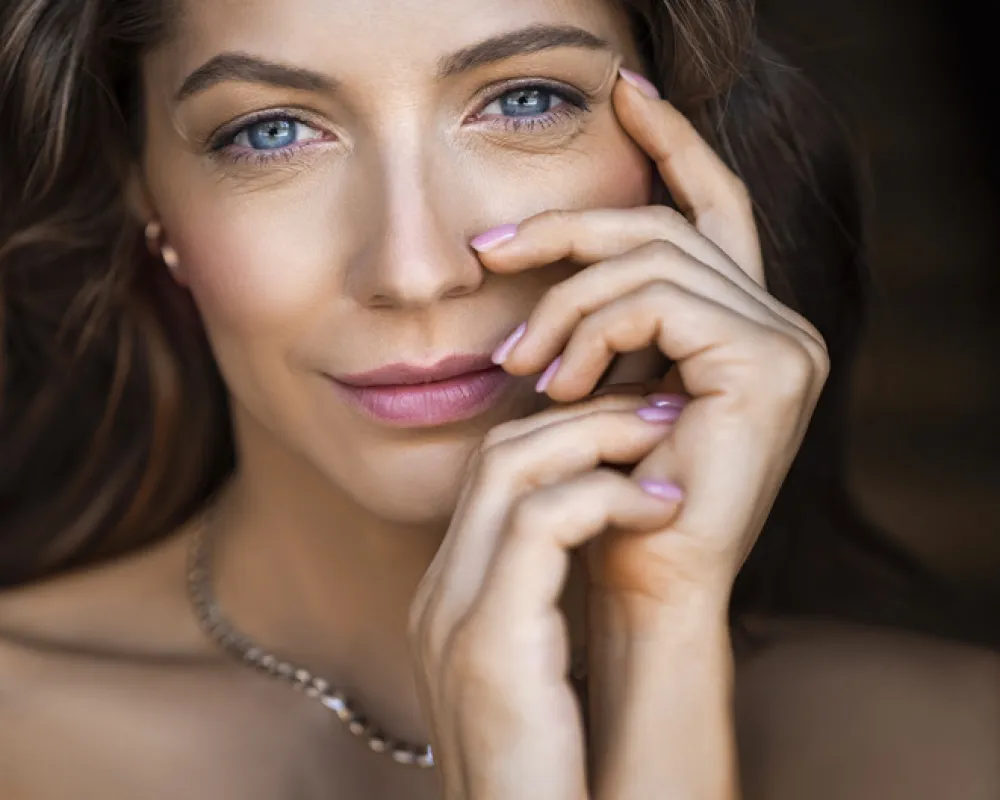 Close-up portrait of a 40 years old blue eyed woman. She touching her face and looking at camera. Sin care concept in the age after 40.