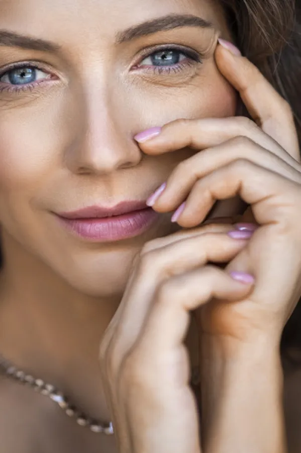 Close-up portrait of a 40 years old blue eyed woman. She touching her face and looking at camera. Sin care concept in the age after 40.