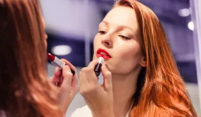 Woman putting lipstick in front of the mirror.