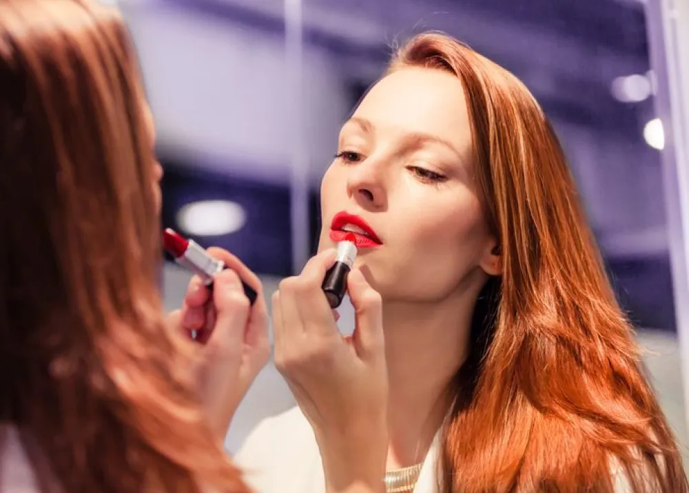 Woman putting lipstick in front of the mirror.