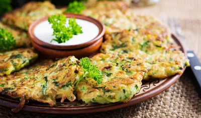 Zucchini fritters. Vegetable vegetarian zucchini pancakes with sauce on wooden background. Healthy food.