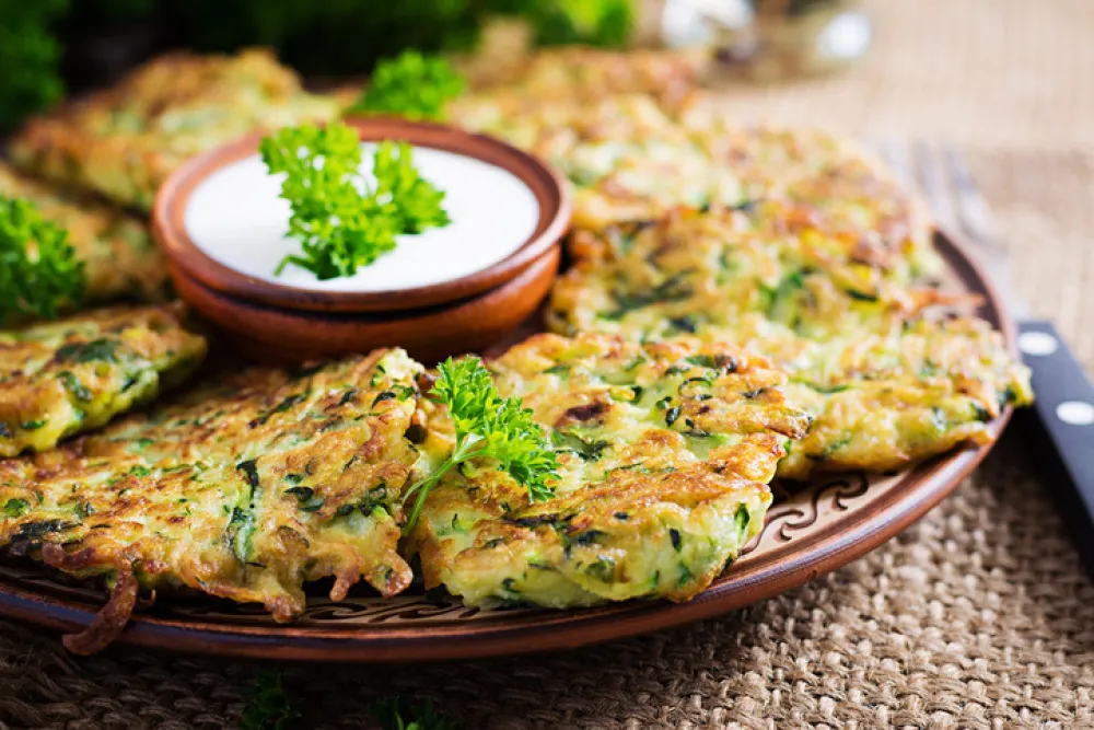 Zucchini fritters. Vegetable vegetarian zucchini pancakes with sauce on wooden background. Healthy food.
