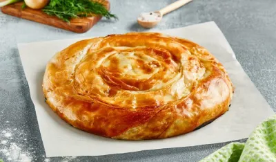Classic turkish pie with meat on wooden board. Composition with burek pie on concrete background with textile and spices. Balkan pie with minced meat in rustic style on gray table