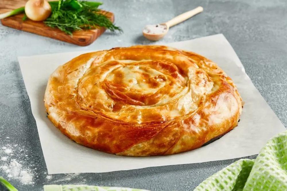 Classic turkish pie with meat on wooden board. Composition with burek pie on concrete background with textile and spices. Balkan pie with minced meat in rustic style on gray table