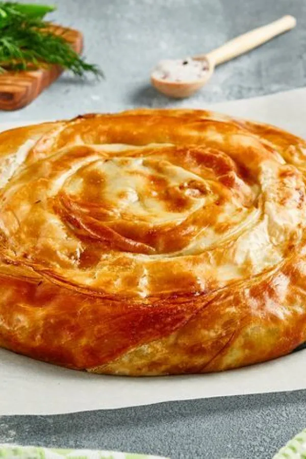 Classic turkish pie with meat on wooden board. Composition with burek pie on concrete background with textile and spices. Balkan pie with minced meat in rustic style on gray table