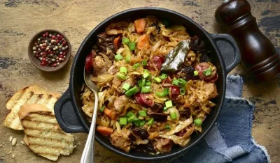 Bigos - traditional dish of polish cuisine,stewed cabbage with meat, sausage and dried mushrooms in a pan on a rustic wooden background. Top view with copy space.