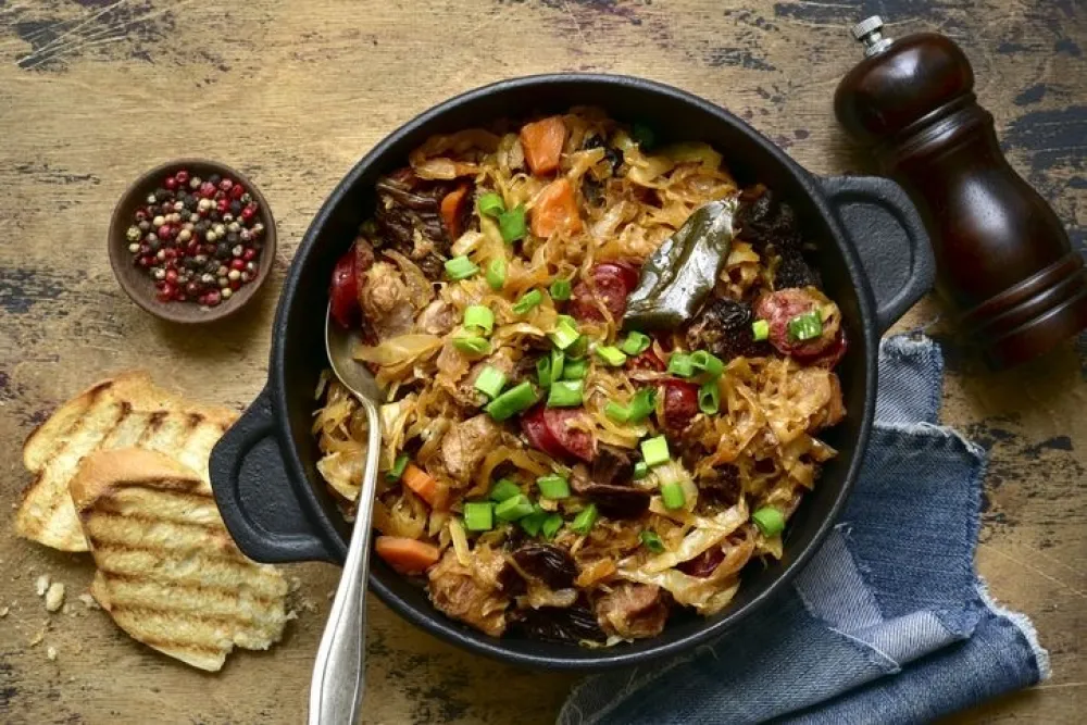Bigos - traditional dish of polish cuisine,stewed cabbage with meat, sausage and dried mushrooms in a pan on a rustic wooden background. Top view with copy space.