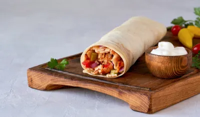 Shawarma with chicken and garlic sauce on wooden board. Closeup