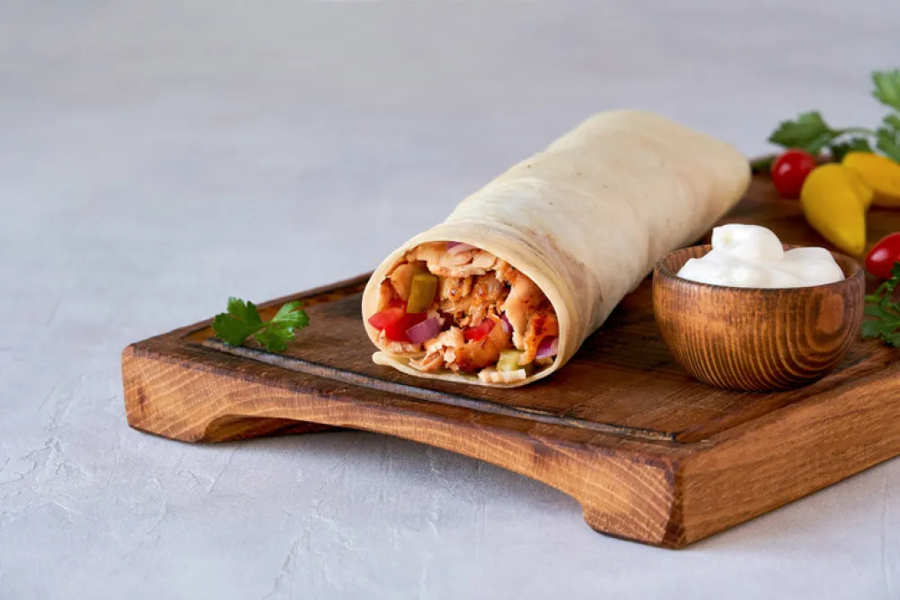 Shawarma with chicken and garlic sauce on wooden board. Closeup