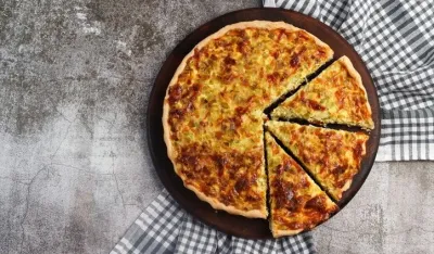 Leek and cheese pie on a round wooden cutting board on a dark grey background. Top view, flat lay