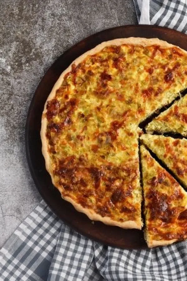 Leek and cheese pie on a round wooden cutting board on a dark grey background. Top view, flat lay