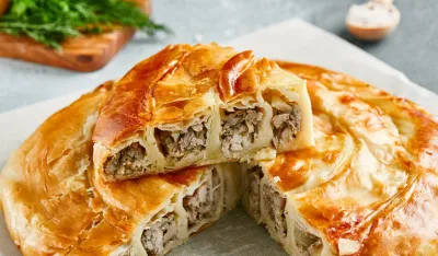 Classic turkish pie with meat on wooden board. Composition with burek pie on concrete background with textile and spices. Balkan pie with minced meat in rustic style on gray table