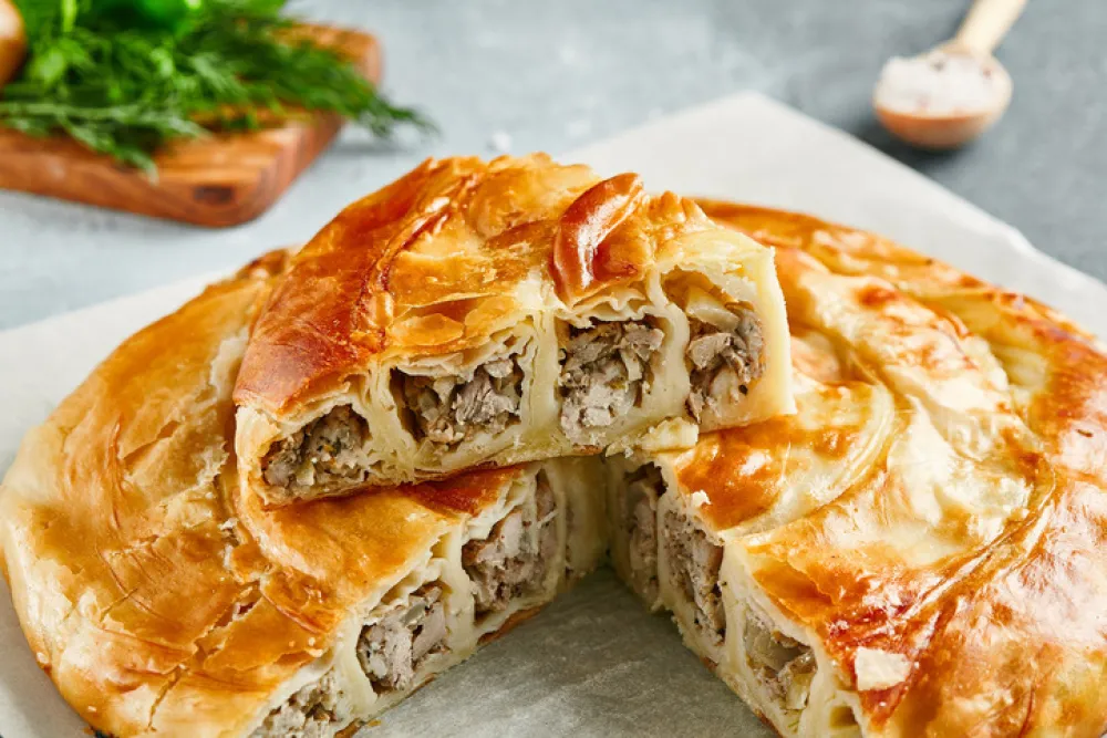 Classic turkish pie with meat on wooden board. Composition with burek pie on concrete background with textile and spices. Balkan pie with minced meat in rustic style on gray table