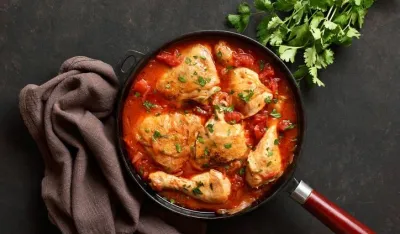 Georgian chicken stew with tomatoes and herbs (chakhokhbili) in cast iron skillet over dark stone background. Baked chicken with tomato vegetable gravy. Top view, flat lay
