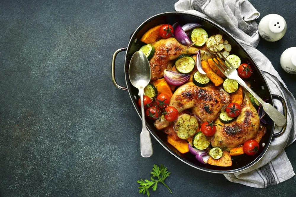 Chicken legs roasted with vegetables in a skillet pan over dark slate,stone or concrete background.Top view.
