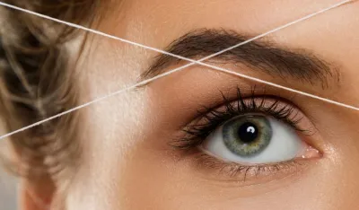 Close-up of female eye with a thread. Eyebrow threading - epilation procedure for brow shape correction